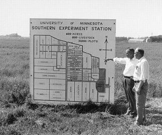 Black and white photo of two men standing next to a large sign showing the borders of the SROC land
